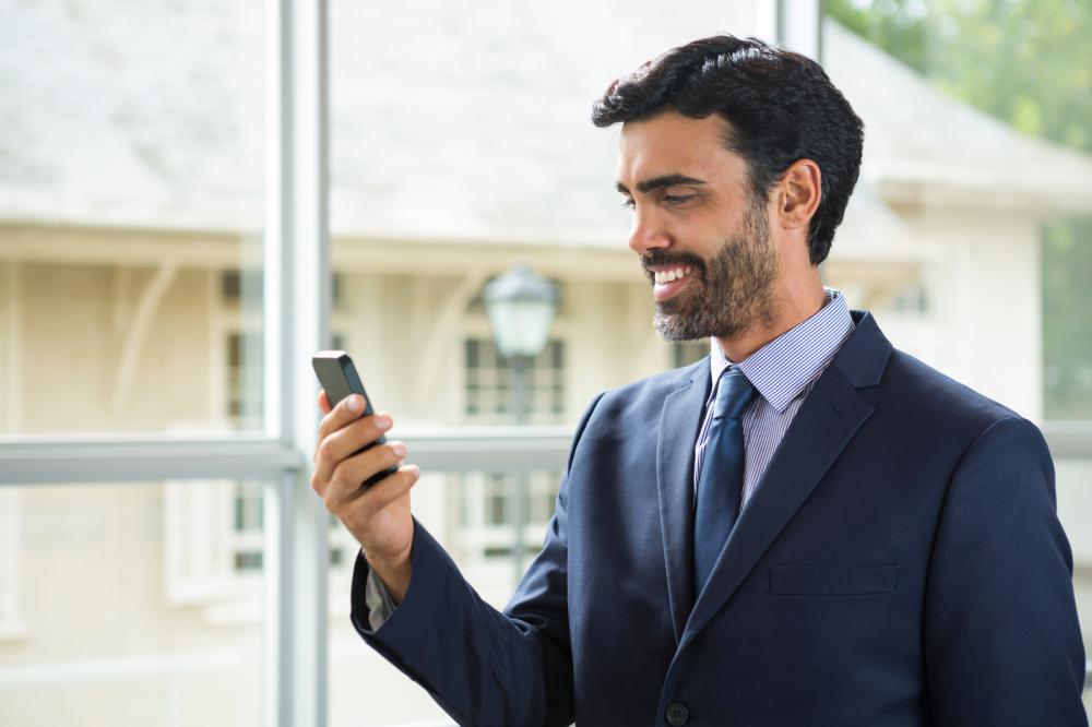 A businessman standing in front of a window using a mobile phone.
